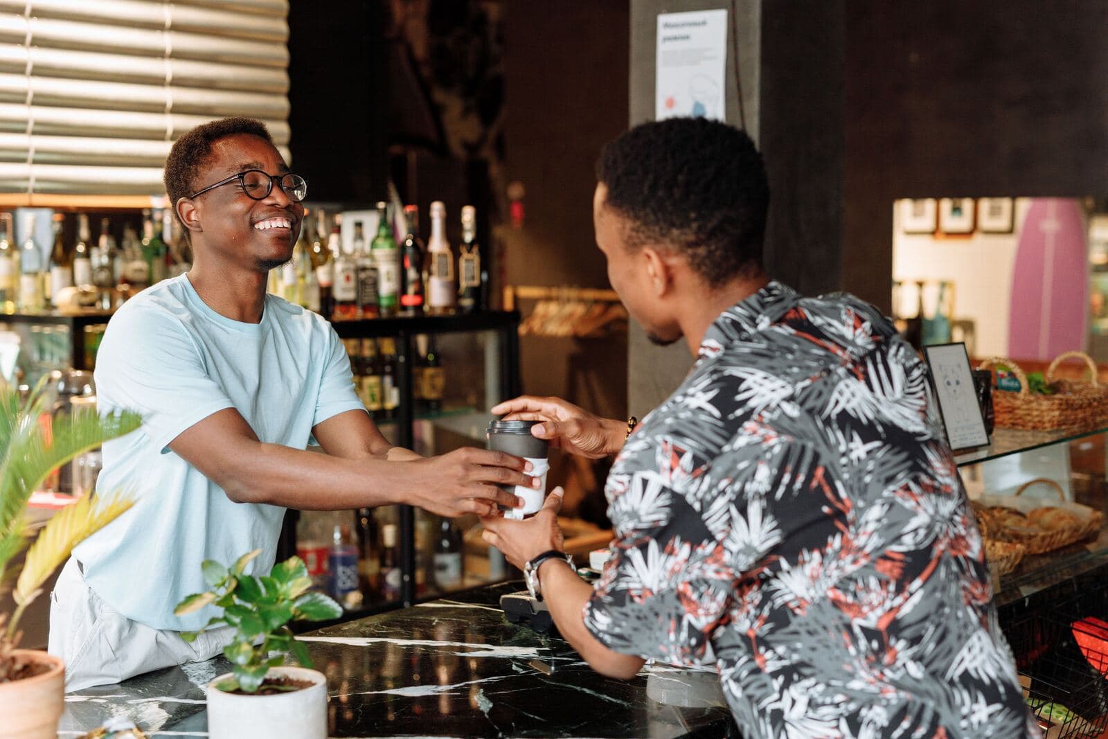 A barista handing a takeaway coffee across the counter to a smiling customer