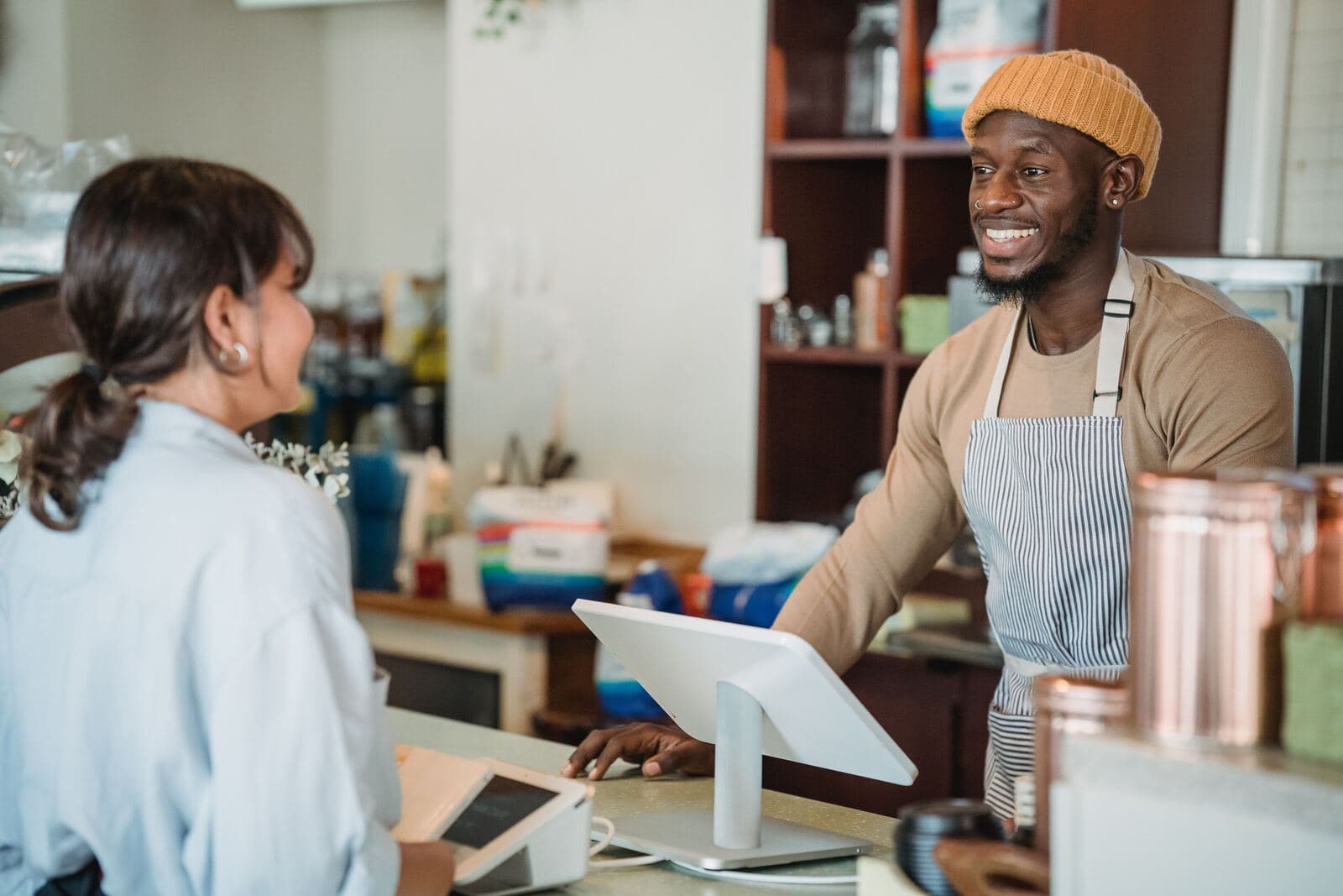 A shop owner in an apron smiling at a customer across the counter, card terminal between them